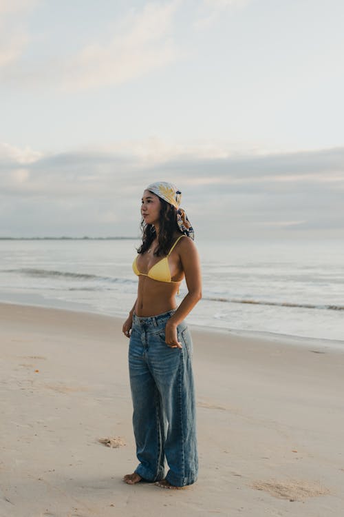 A woman in a yellow hat and blue jeans standing on the beach
