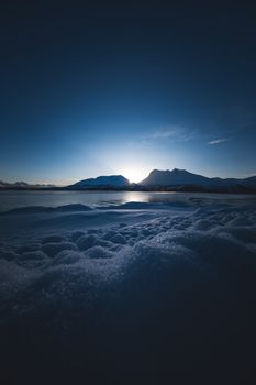 A breathtaking twilight scene with a snowy foreground and mountains silhouetted against a setting sun.
