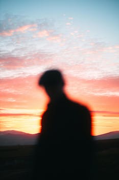 A blurred silhouette of a person against a colorful sunrise with mountains in the background.