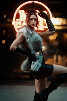 A fashionable woman poses confidently in a neon-lit urban environment at night.