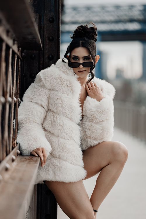 Free Fashionable woman in white fur posing outdoors with sunglasses. Urban background. Stock Photo