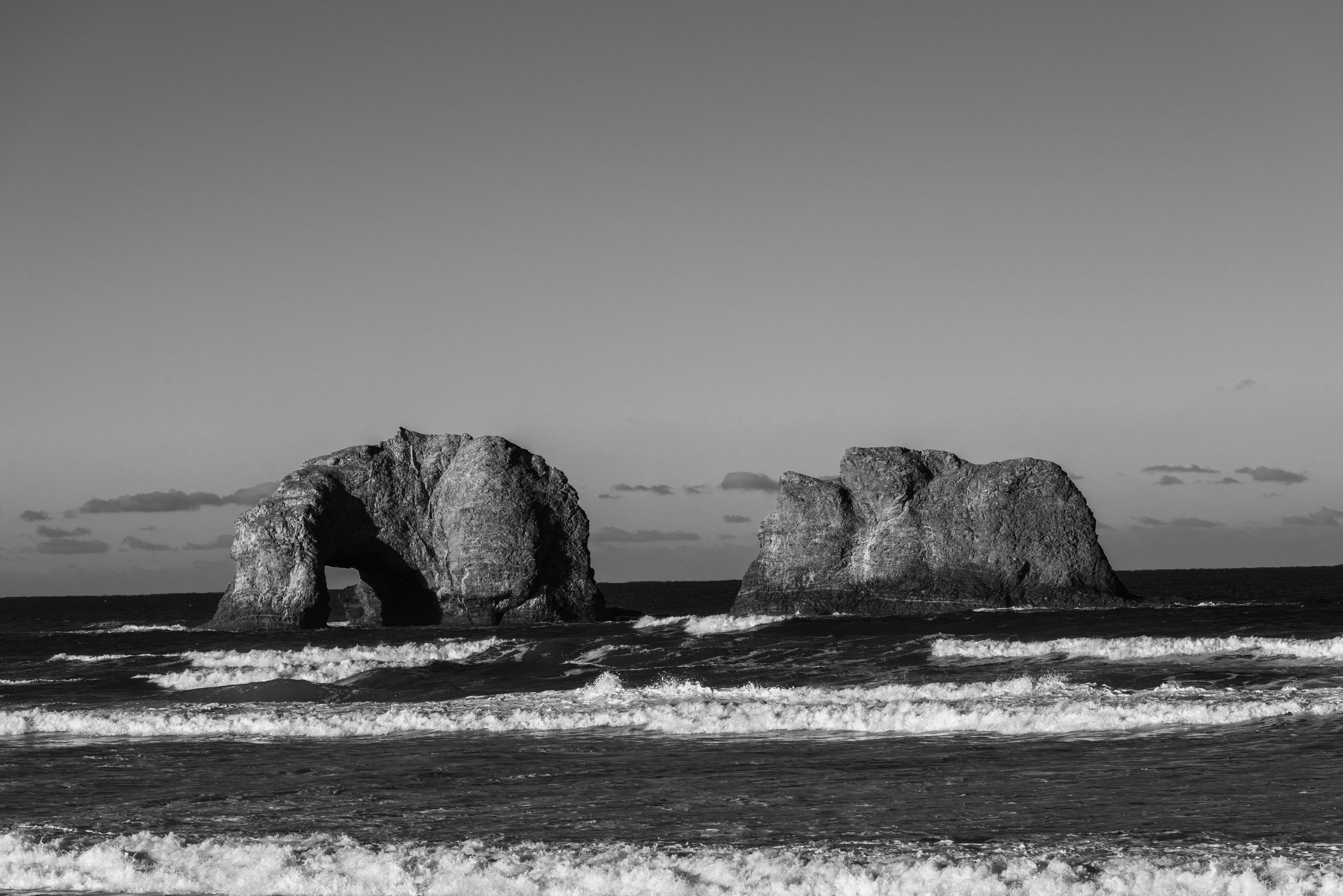 Dramatic black and white photo of Twin Rocks at Rockaway Beach, capturing ocean waves and rock formations.