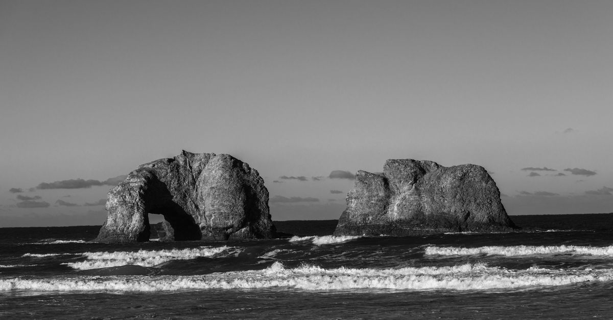 Dramatic black and white photo of Twin Rocks at Rockaway Beach, capturing ocean waves and rock formations.