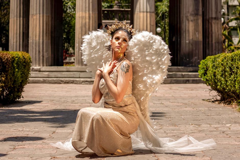 A woman dressed as an angel with wings kneels outdoors, embodying grace and elegance.