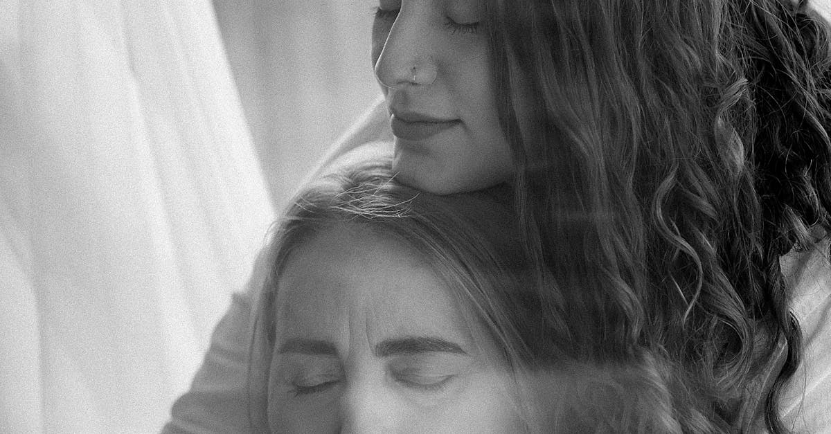 Touching black and white portrait of a mother and daughter embracing warmly near a window.