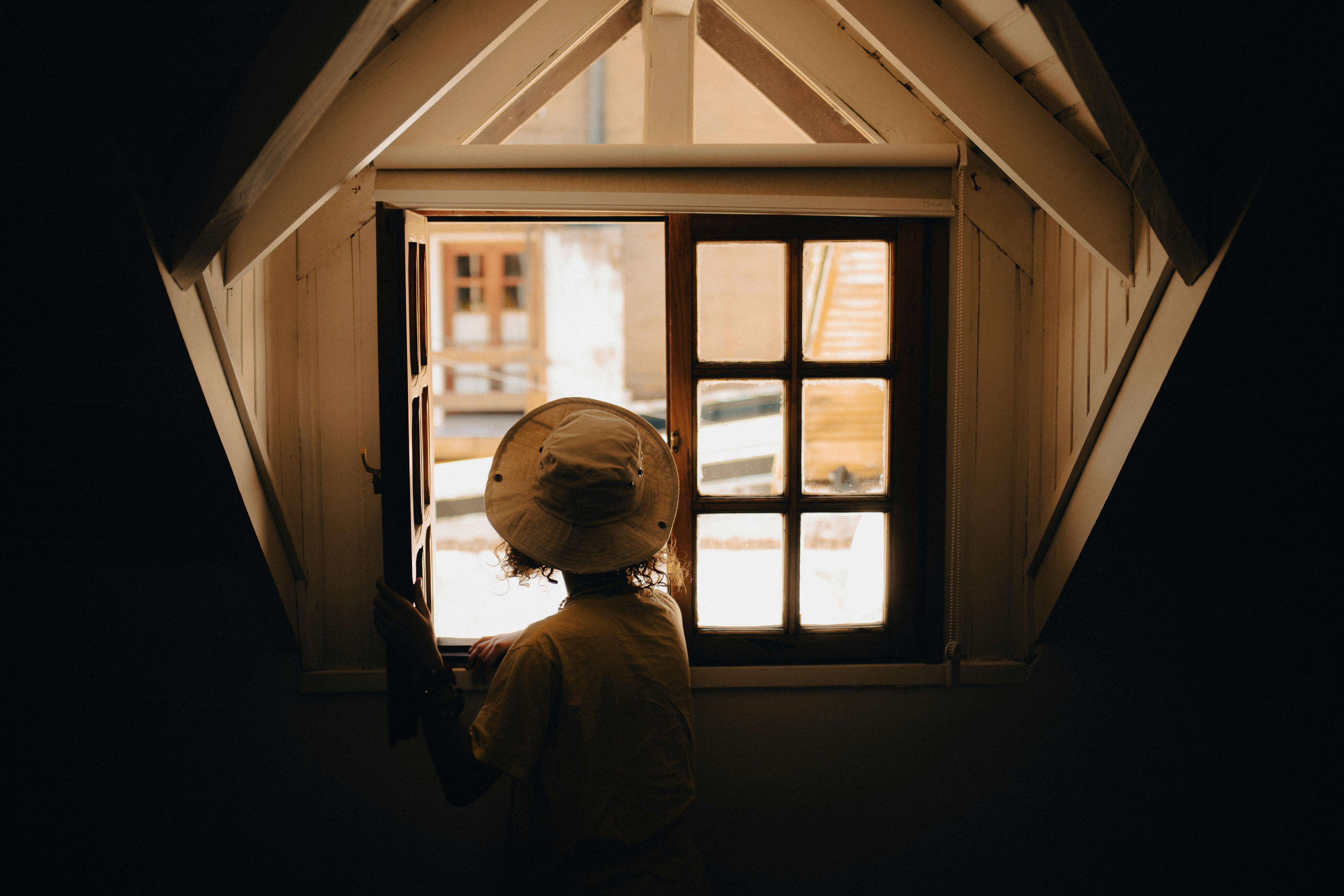 A person gazes out of a rustic window, creating a contrast of light and dark inside a cozy space.