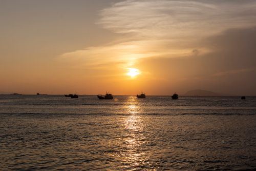 Free Beautiful ocean sunset with several boats silhouetted against the vibrant sky and serene water reflections. Stock Photo