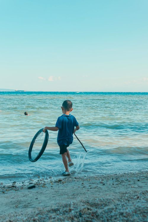 Free A child enjoys playing with a ring along the shoreline of a sunny beach. Perfect summer vacation scene. Stock Photo
