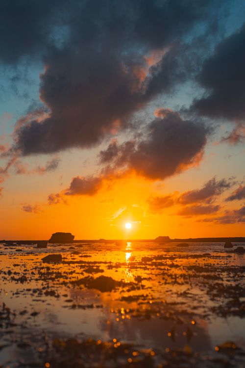 Free Stunning sunset over a calm sea, casting vivid reflections under dramatic clouds. Stock Photo