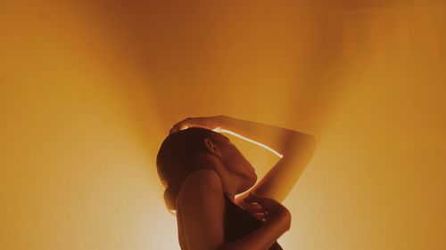 Free Eloquent pose of a woman in dramatic lighting against a warm background. Stock Photo