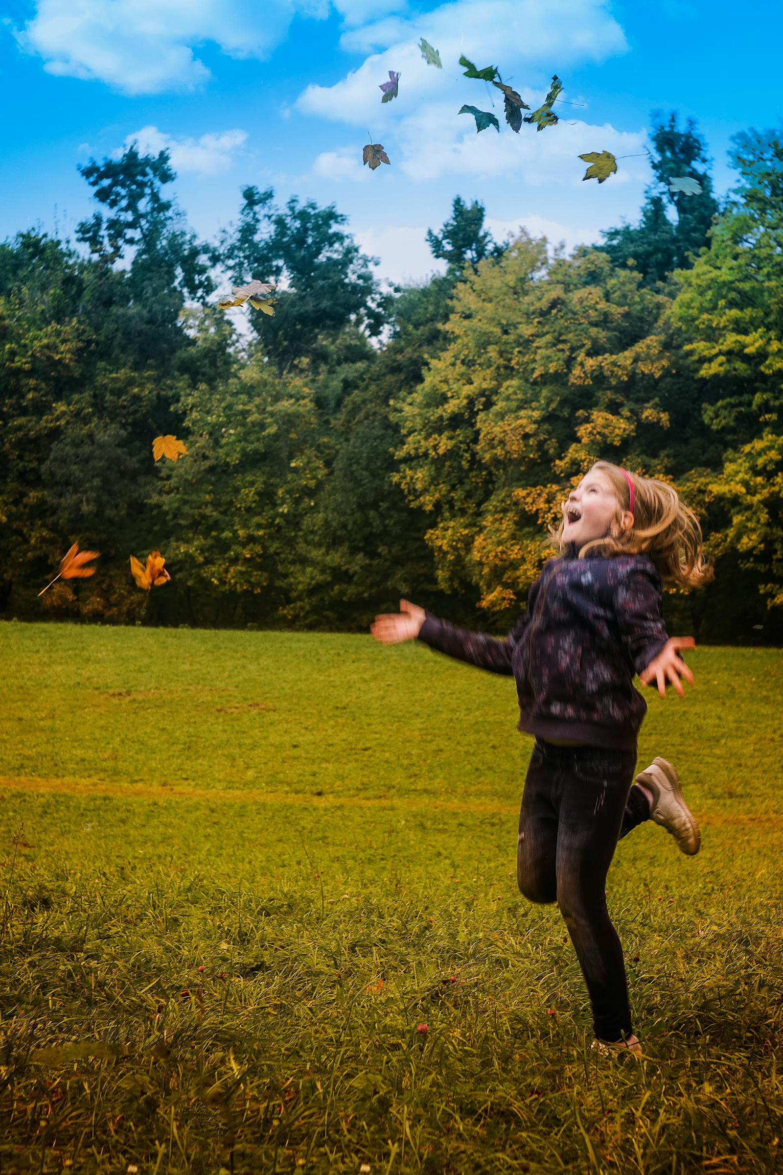 Young girl joyfully playing in a green park surrounded by trees and falling autumn leaves—capturing the family-friendly, nature-rich lifestyle of Arbor Creek in Saskatoon.