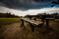 在宁静的公园里，木制野餐桌伫立在戏剧性的多云天空下