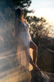 一名女子身穿飘逸连衣裙，站在自然光线下的岩石上，捕捉到了这一平静的时刻