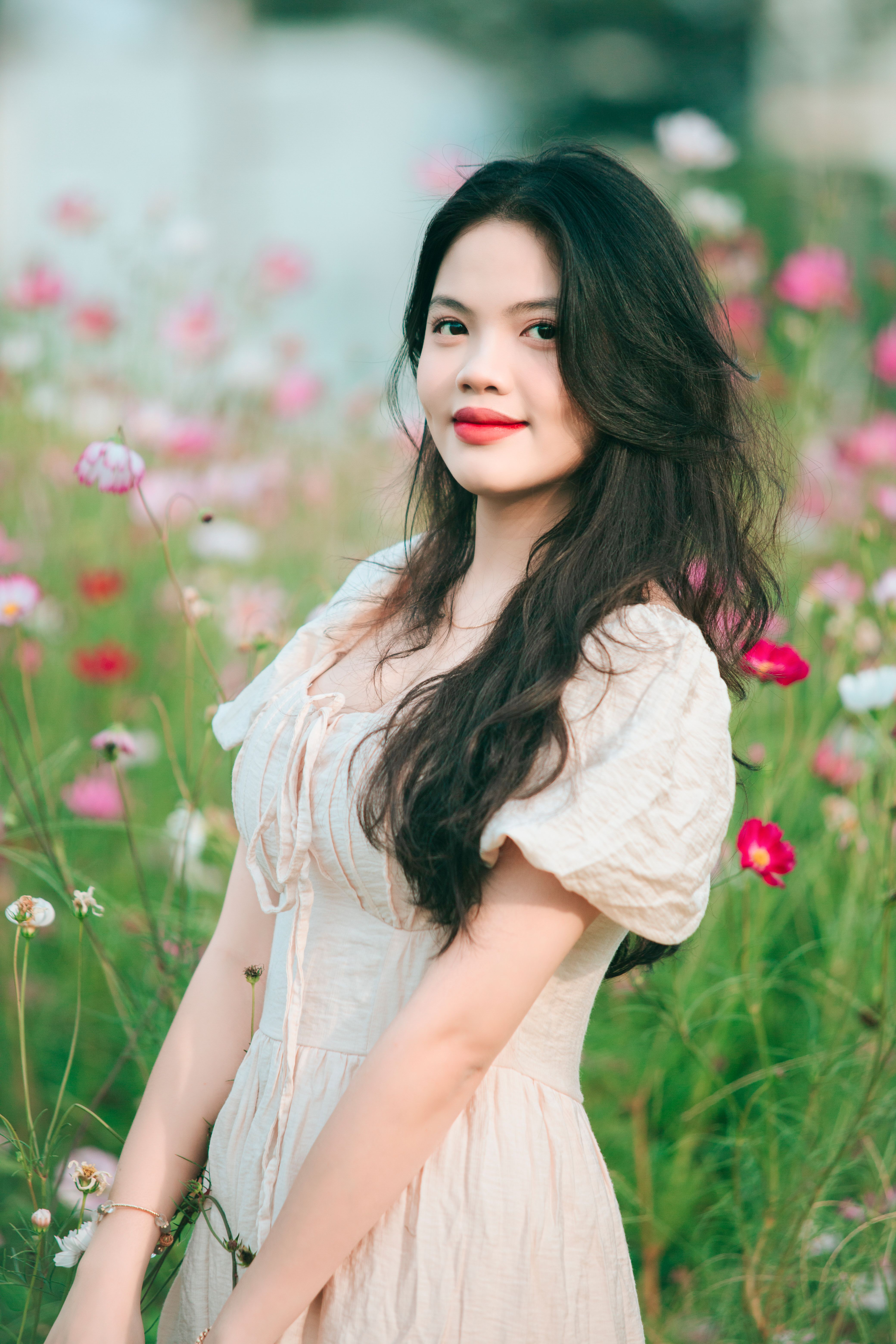 Portrait of a smiling woman with long hair in a floral meadow.