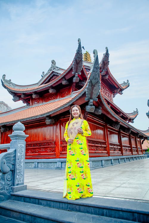 A woman in yellow dress standing in front of a chinese temple