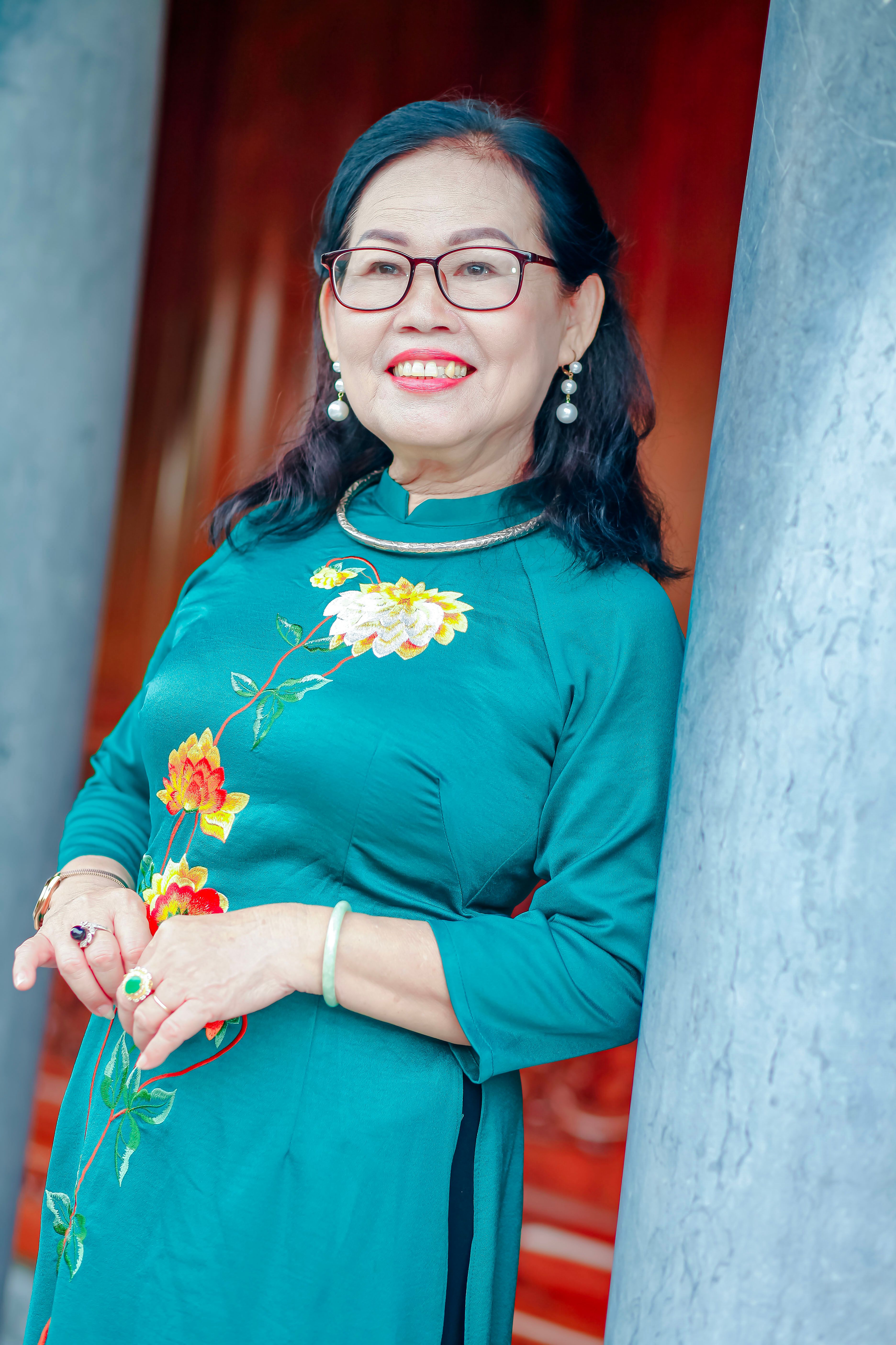 A smiling middle-aged woman in a vibrant green traditional dress posing near stone pillars.