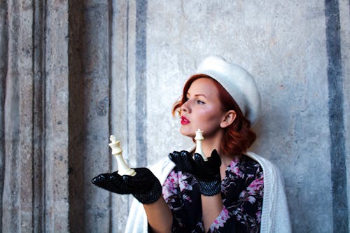 A woman in a hat and gloves holding a chess piece