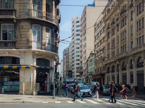 Free A bustling city intersection with pedestrians crossing and historic architecture lining the street. Stock Photo