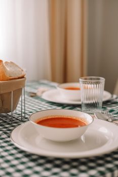 Warm tomato soup served on a table with bread basket in a cozy indoor setting.