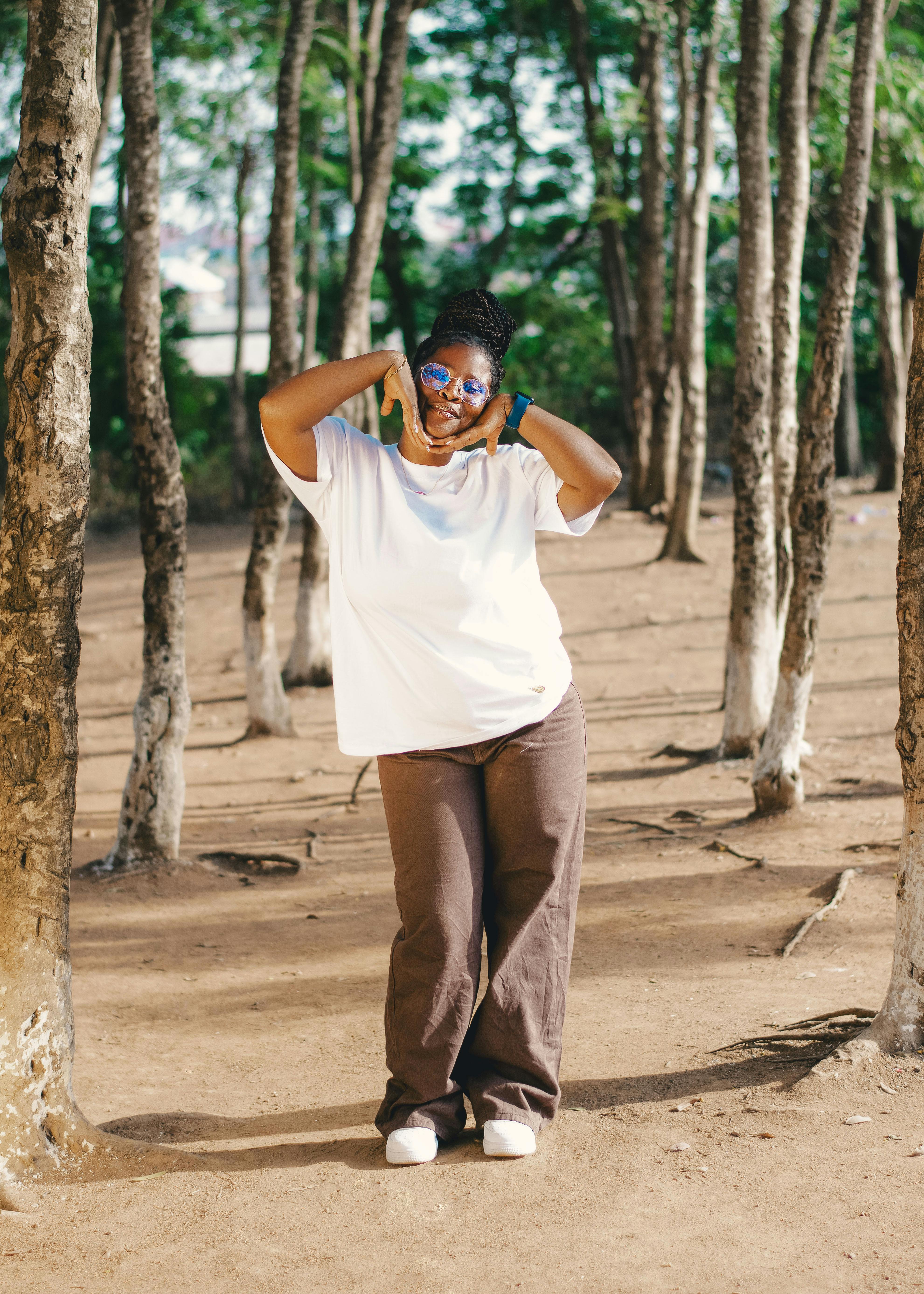 a woman in a white shirt and brown pants standing in a forest