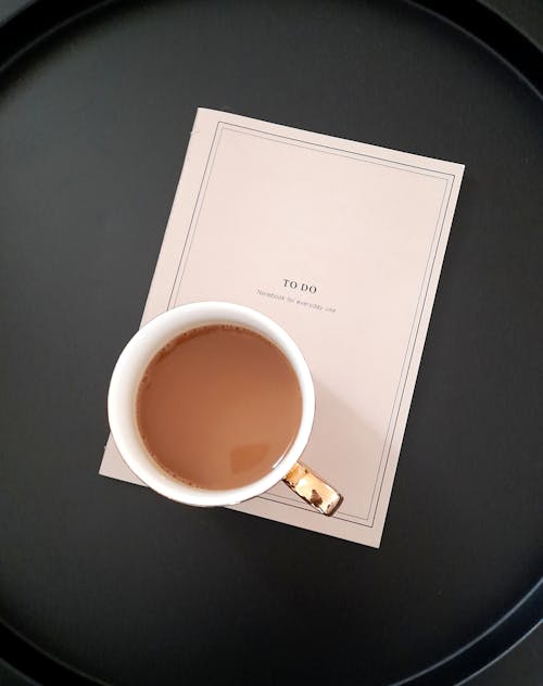 A cup of coffee sits on a tray next to a book