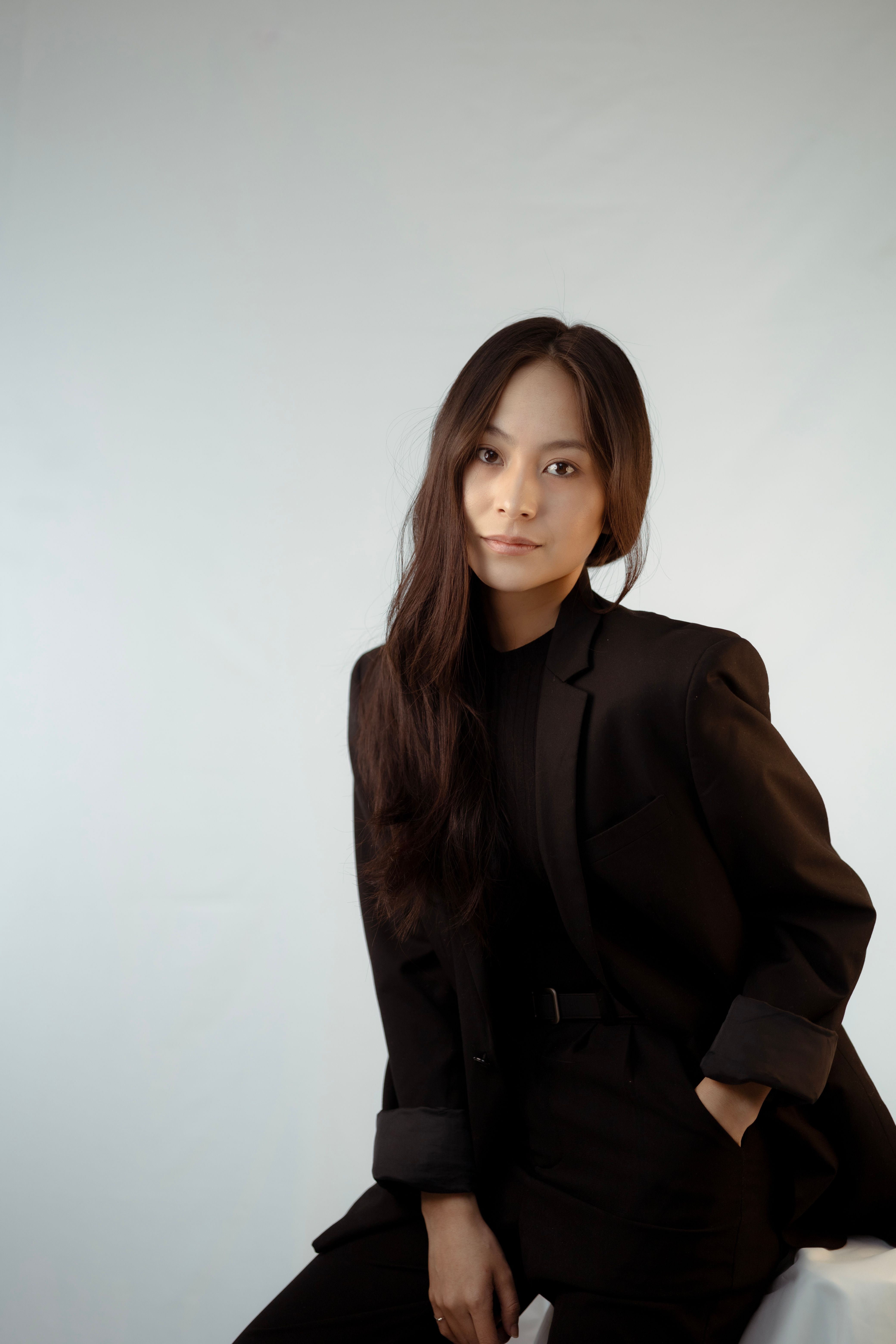 Sophisticated portrait of an Asian businesswoman in a black suit with long brown hair, exuding elegance and professionalism.