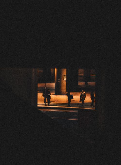 Free Silhouetted pedestrians stand under streetlights in a dimly lit urban area at night. Stock Photo