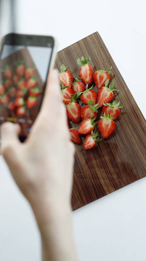 A person taking a picture of strawberries on a wooden cutting board