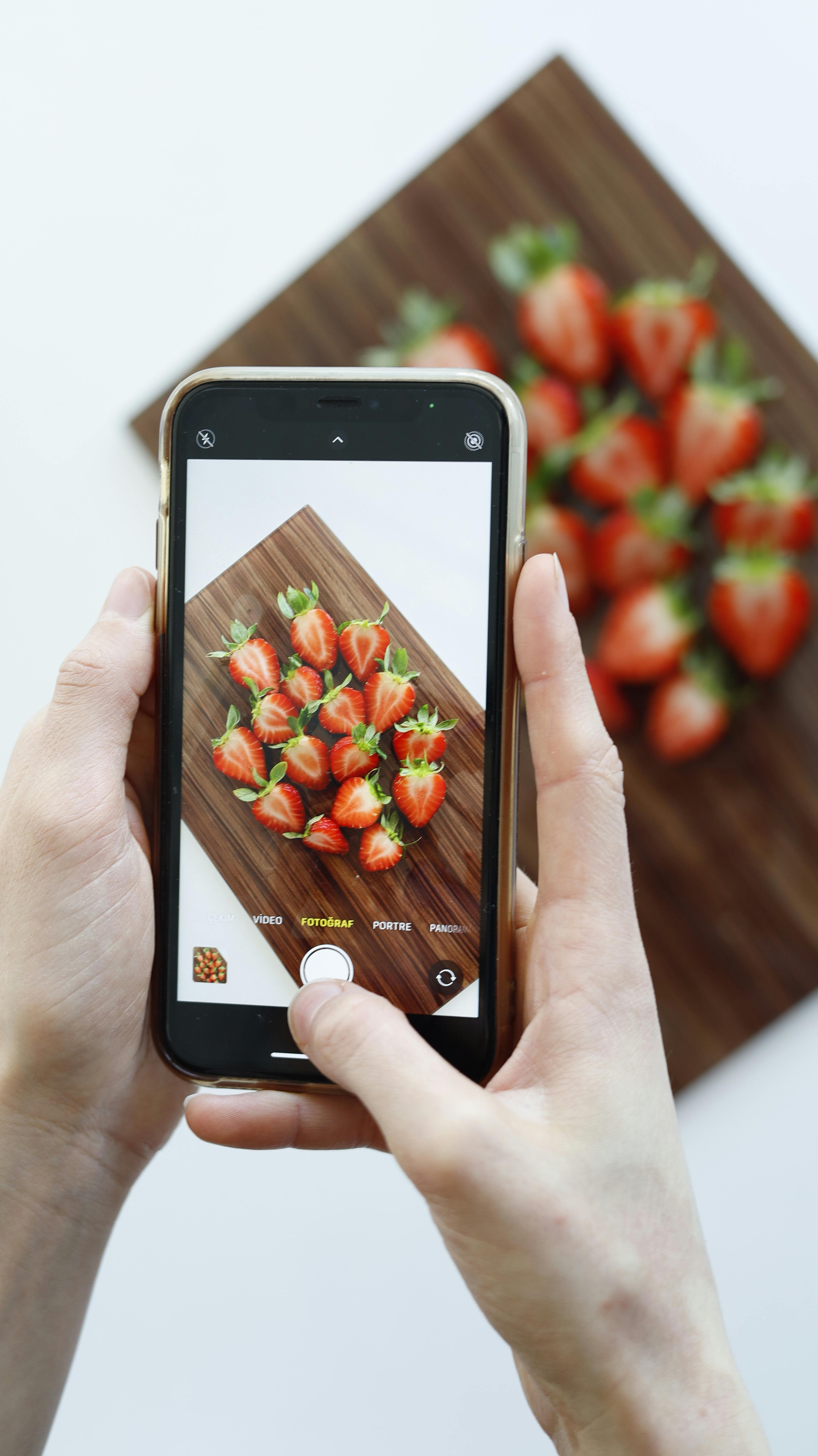 Hands photographing strawberries on a cutting board using a smartphone.