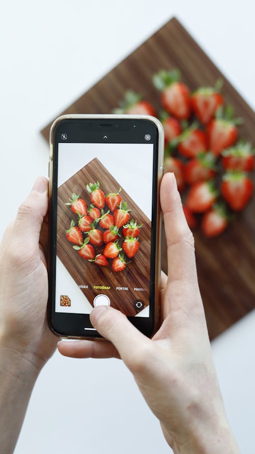 A person taking a photo of strawberries on a wooden cutting board