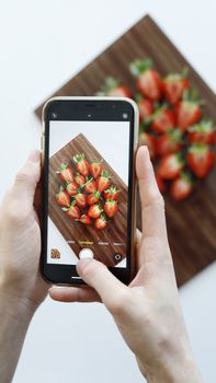 Hands photographing strawberries on a cutting board using a smartphone.