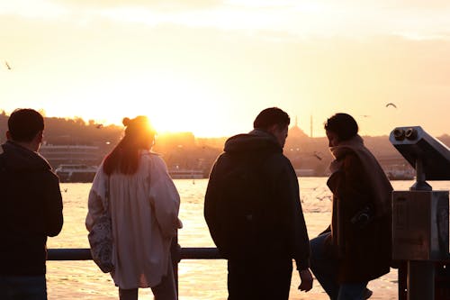 A group of people standing on a pier looking at the sunset