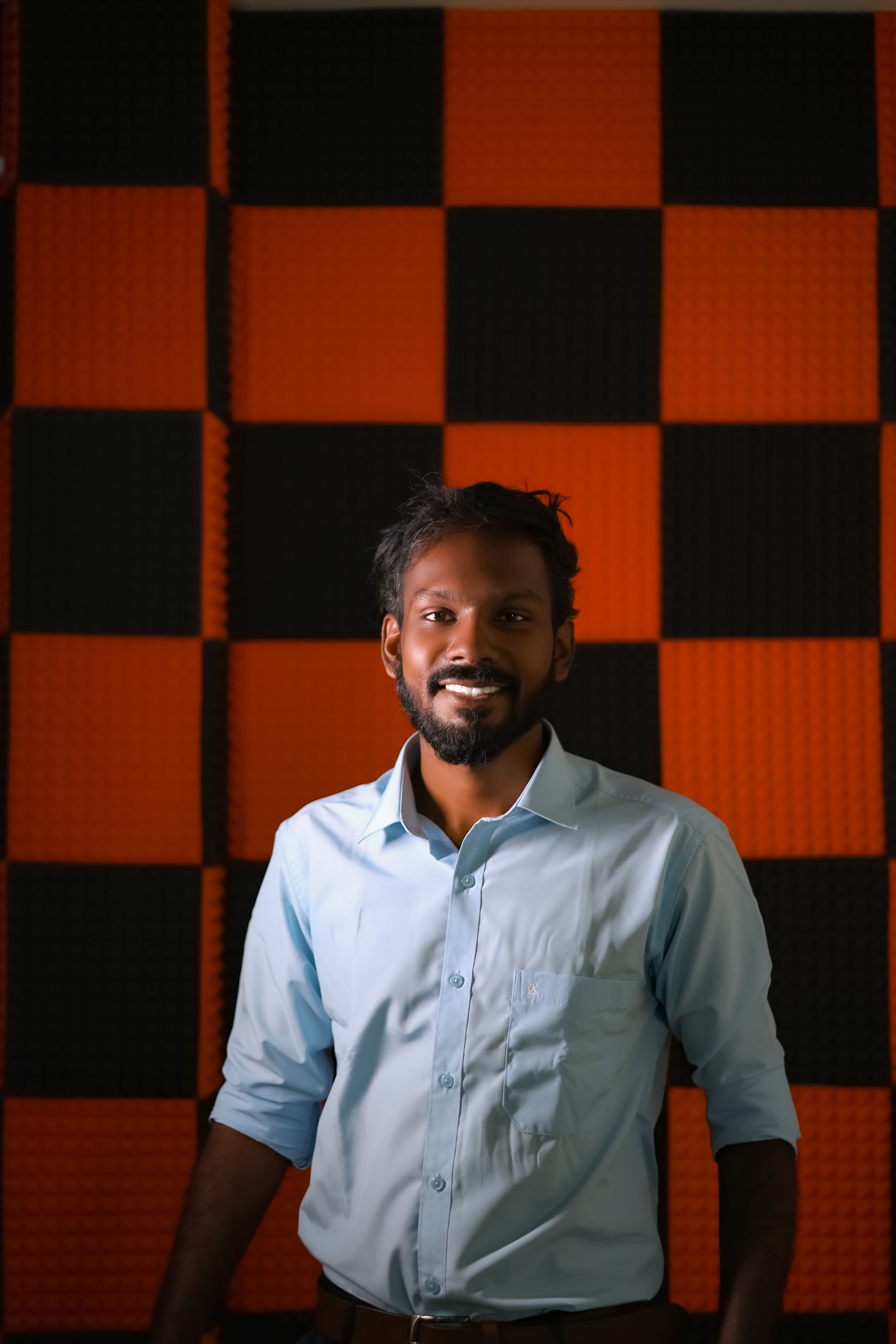 Portrait of a smiling man standing against a red and black checkered background.