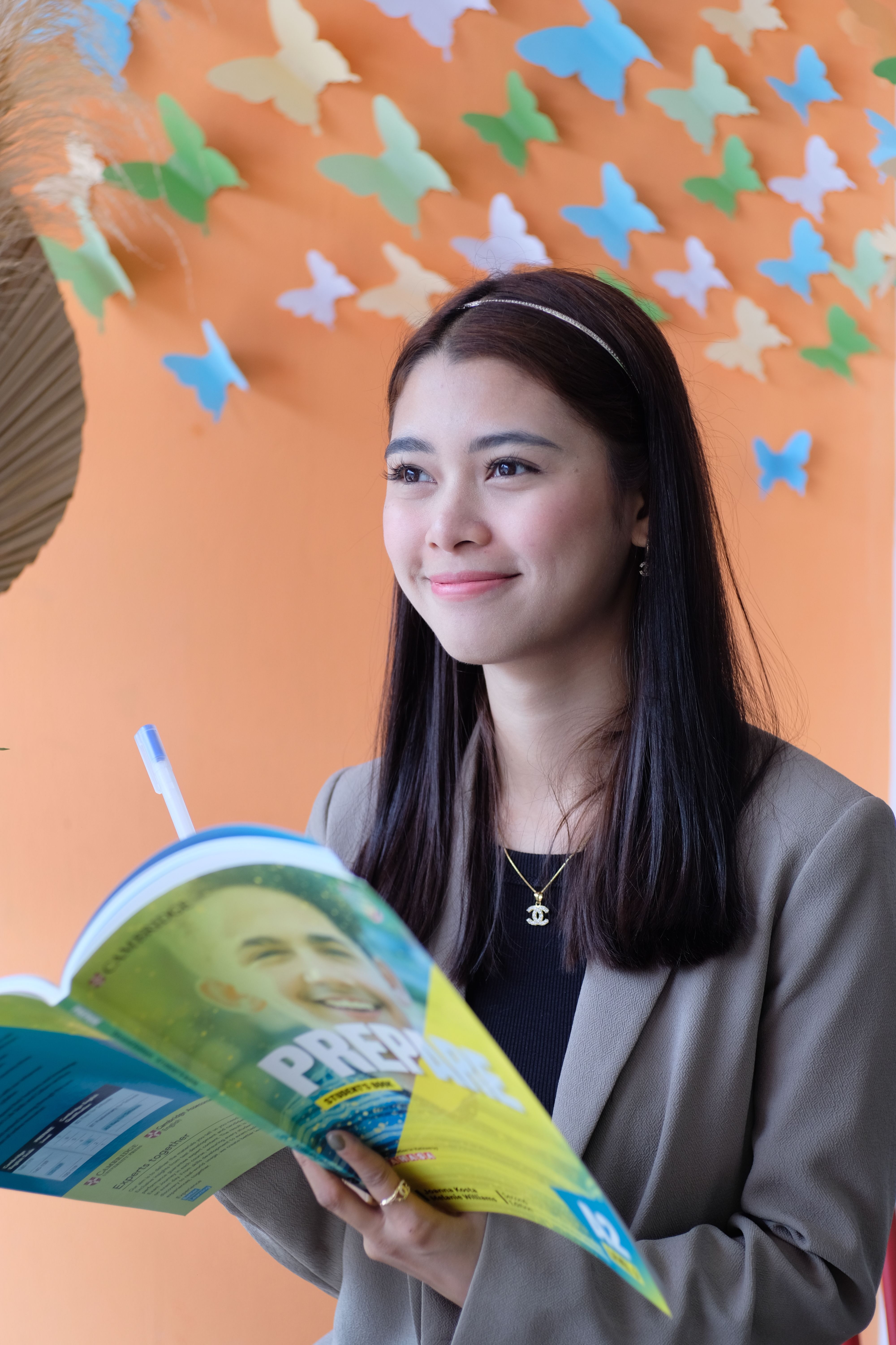 Portrait of a smiling young woman holding a book indoors with colorful butterfly decorations.