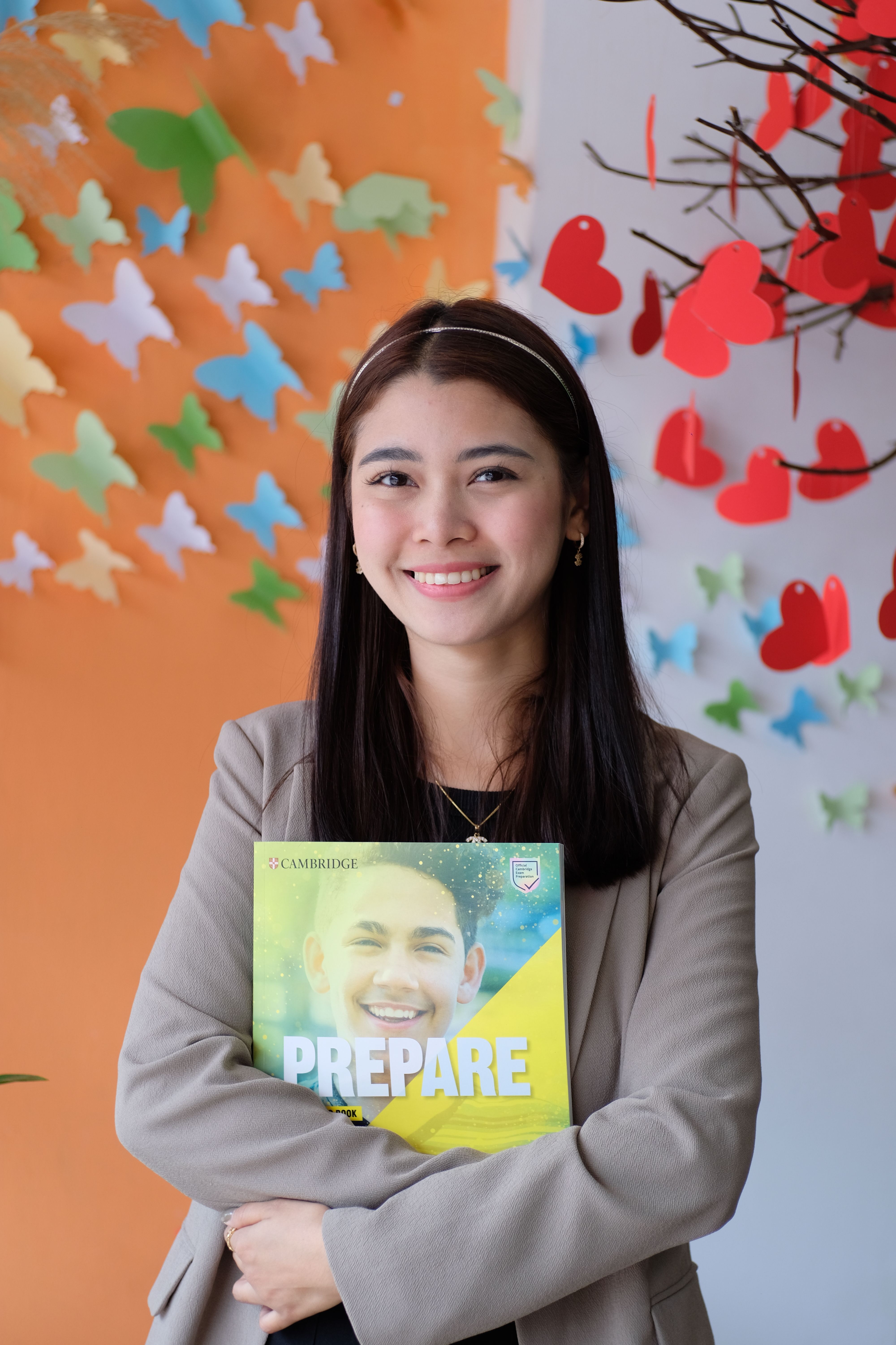 A smiling woman holding a book with colorful decorations in the background.