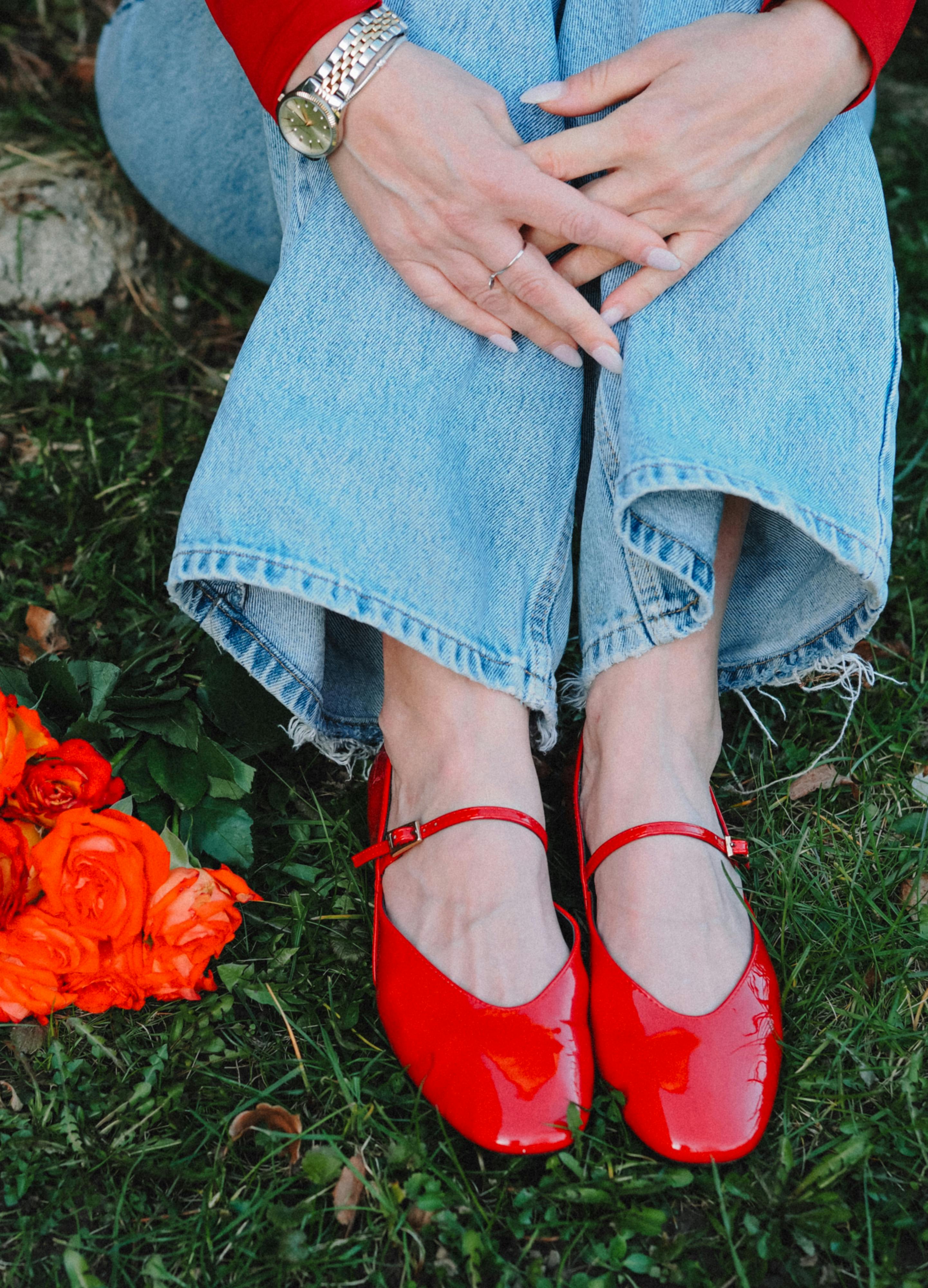 A close-up of red shoes and jeans on grass, with orange flowers nearby.