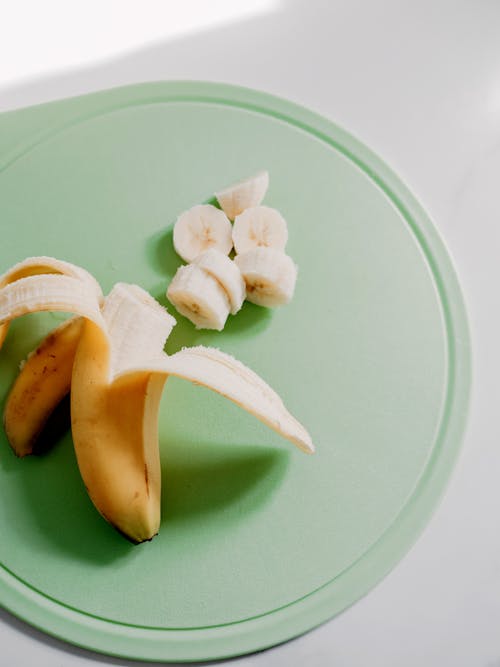 A banana and a piece of fruit on a green cutting board