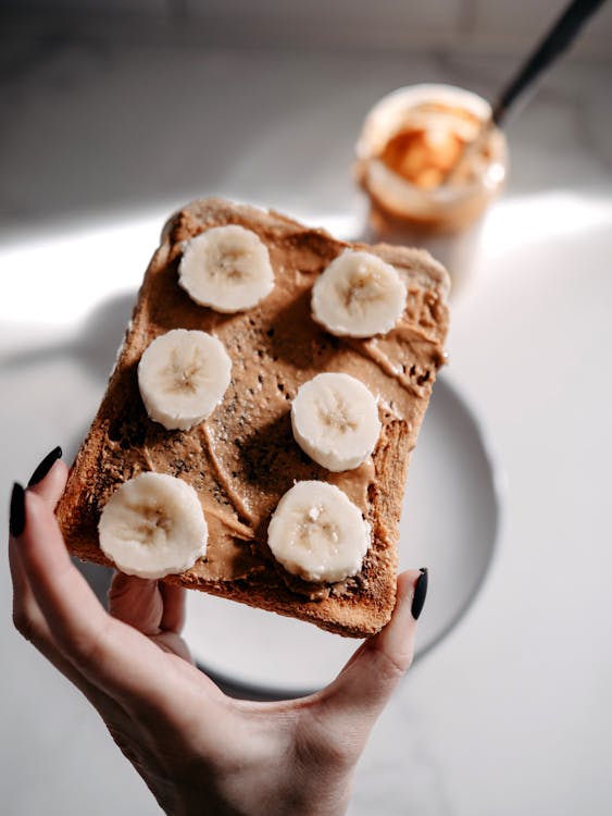 A person holding a piece of toast with peanut butter and bananas