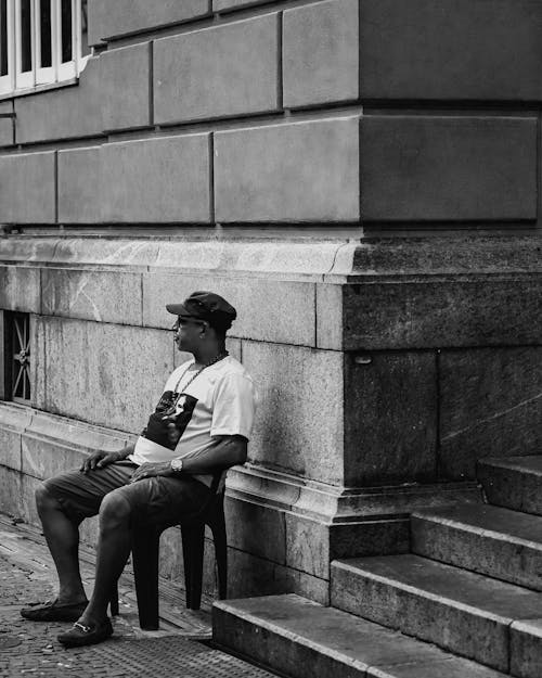 Man in Cap and T-shirt Sitting on Sidewalk