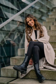 A stylish woman in Berlin showcasing modern fashion with a smile, beige coat, and black boots.