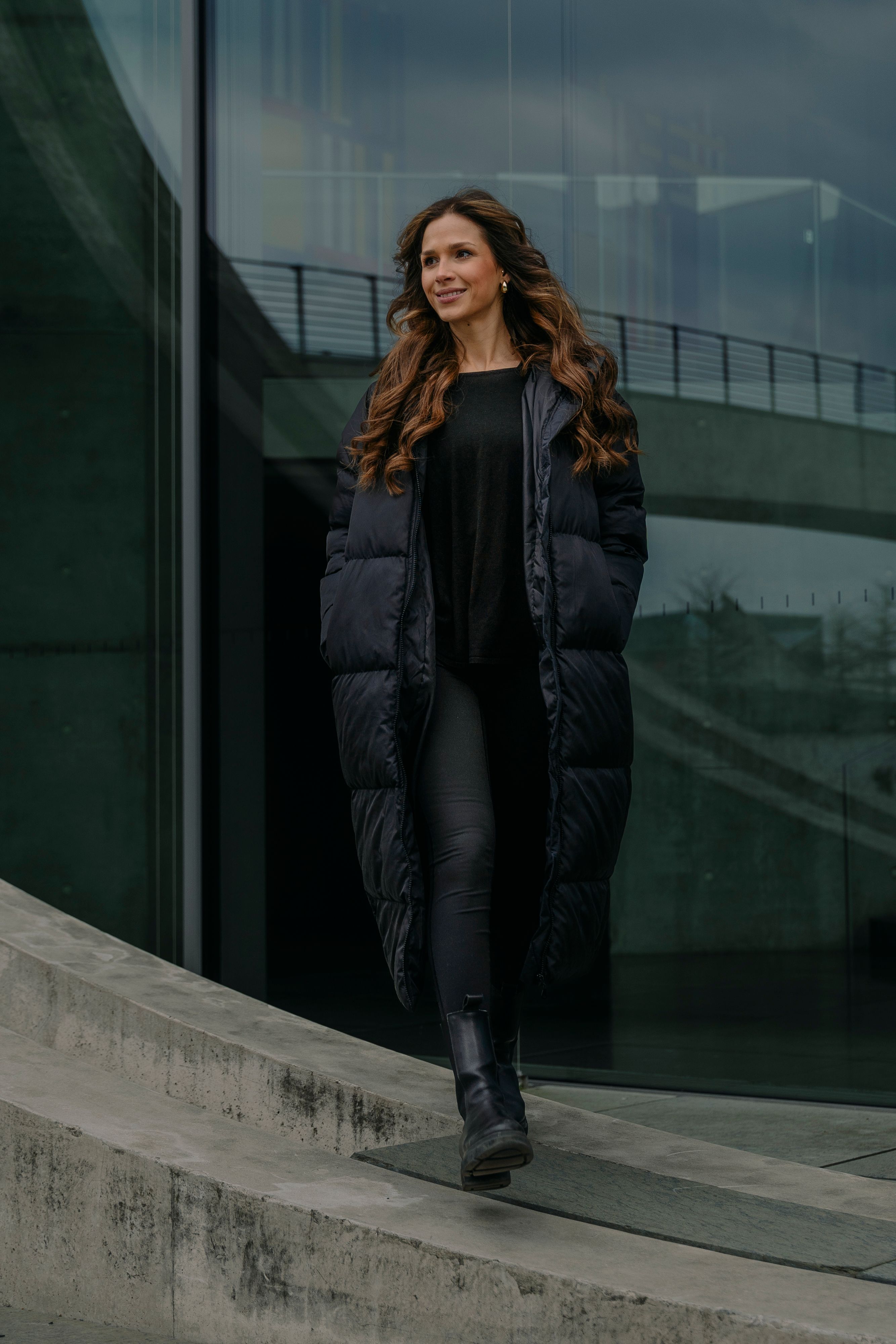 Elegant woman in black fashion outfit walking outside modern building in Berlin, Germany.