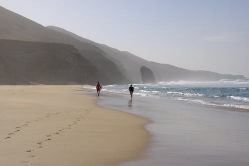 Two people walking on a sandy beach with the ocean in the background
