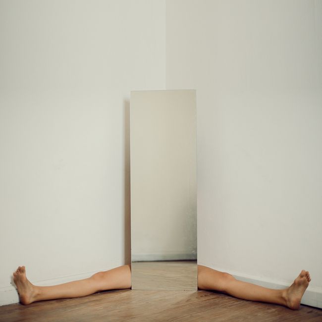 Contemporary minimalist art of human legs and a mirror in a stark white room.