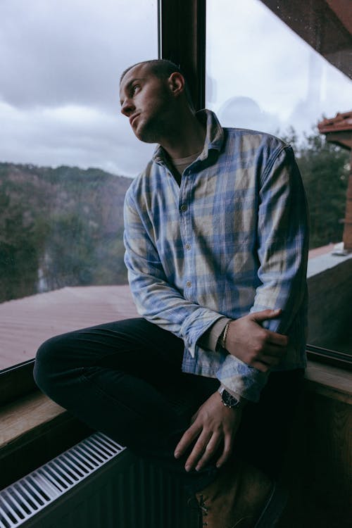 Man in a Checkered Shirt Sitting by a Window