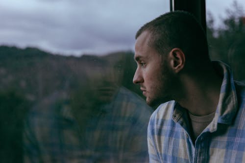 Man in a Checkered Shirt Sitting by a Window 