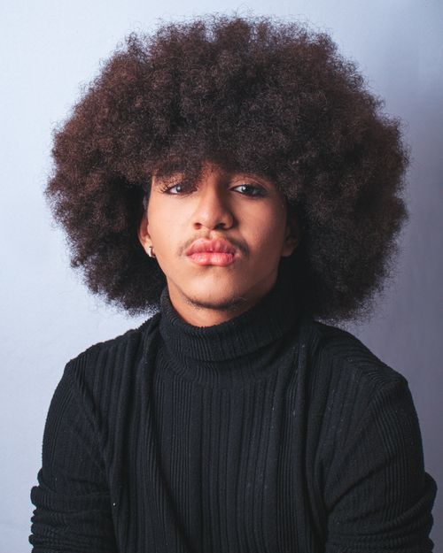 Free Portrait of a fashionable young man with an afro hairstyle wearing a black turtleneck against a simple background. Stock Photo