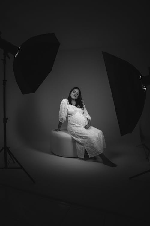 A pregnant woman sitting on a white chair in a studio