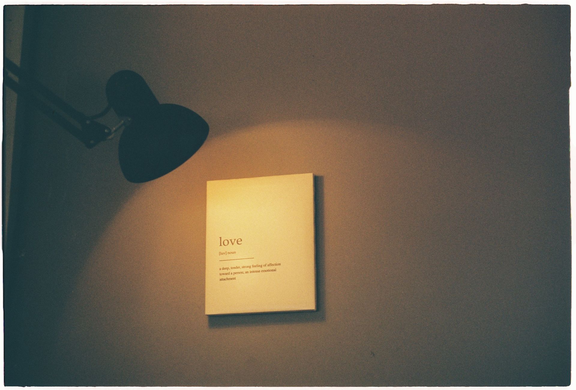 A warm-lit room showcasing a board with the definition of love illuminated by a lamp.