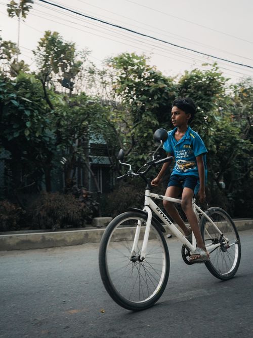 Free A young boy in a blue shirt skillfully rides a bicycle down a quiet city street. Stock Photo