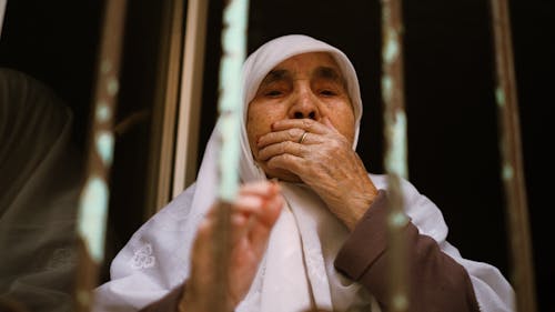 A woman in a white headscarf looks out of a window